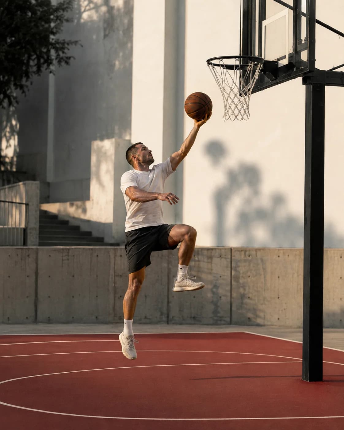 A basketball player rising for a layup above a red outdoor court